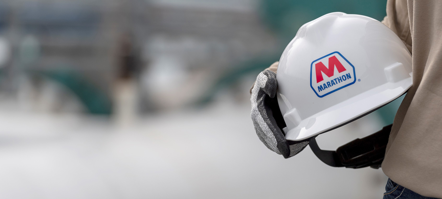A hand holding a white safety helmet with the red and blue Marathon logo