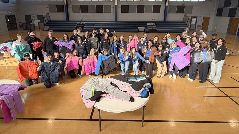 Large group of people pose together indoors with coats.