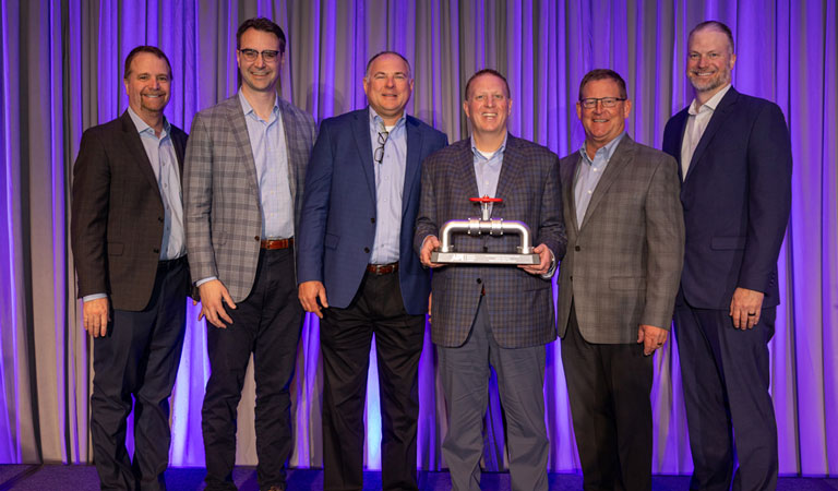 The MPL C-suite standing on a stage holding a pipeline model with lavender curtains behind them