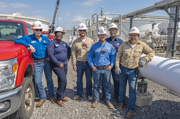 MPL terminal workers standing together smiling between a white pipe and a red truck