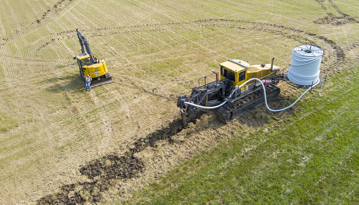An irrigation tractor laying tubing in a field next to an excavator