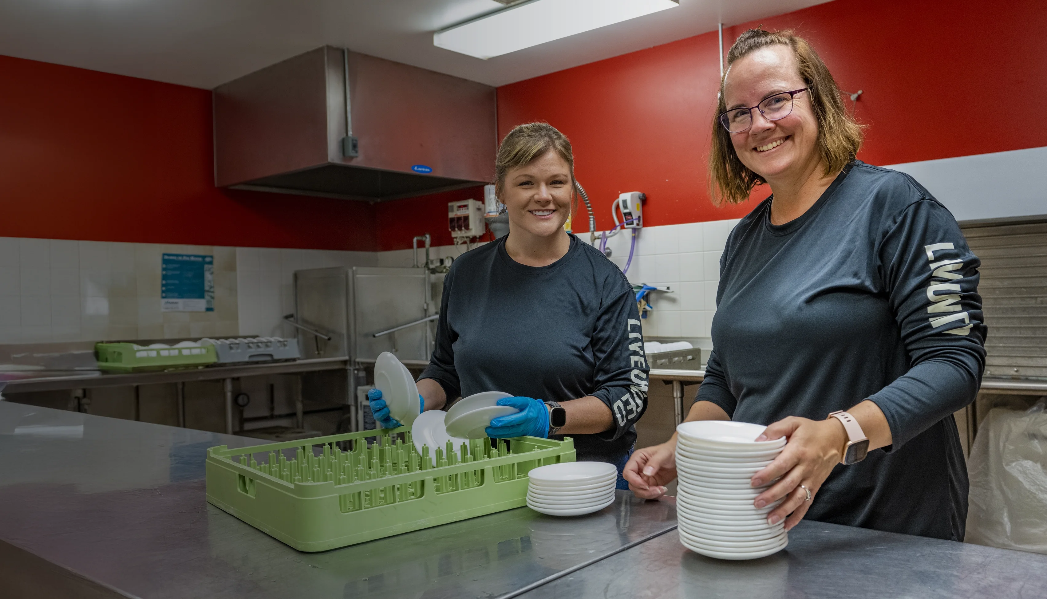 Two MPL employees volunteering in a kitchen, cleaning and drying dishes