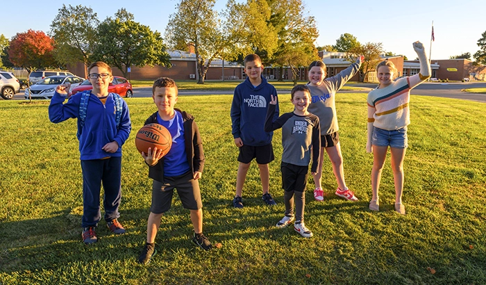 Children waving and holding basket balls on the lawn outside of an elementary school at dusk