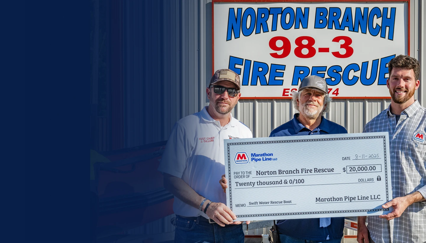 Group of men from Marathon Pipe Line and local fire and police departments standing together in a conference room, holding a large ceremonial check for $9,500 made out to Shawnee Fire/Police
