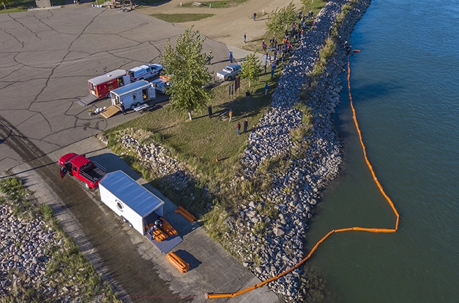 An aerial view of trucks unloading inflatable barriers along a rocky shoreline