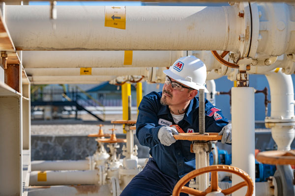 An MPL terminal worker looking up at a white pipe while turning an orange wheel on a valve
