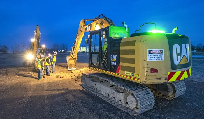 Construction workers standing together at night looking at where an excavator broke ground for a new pipeline