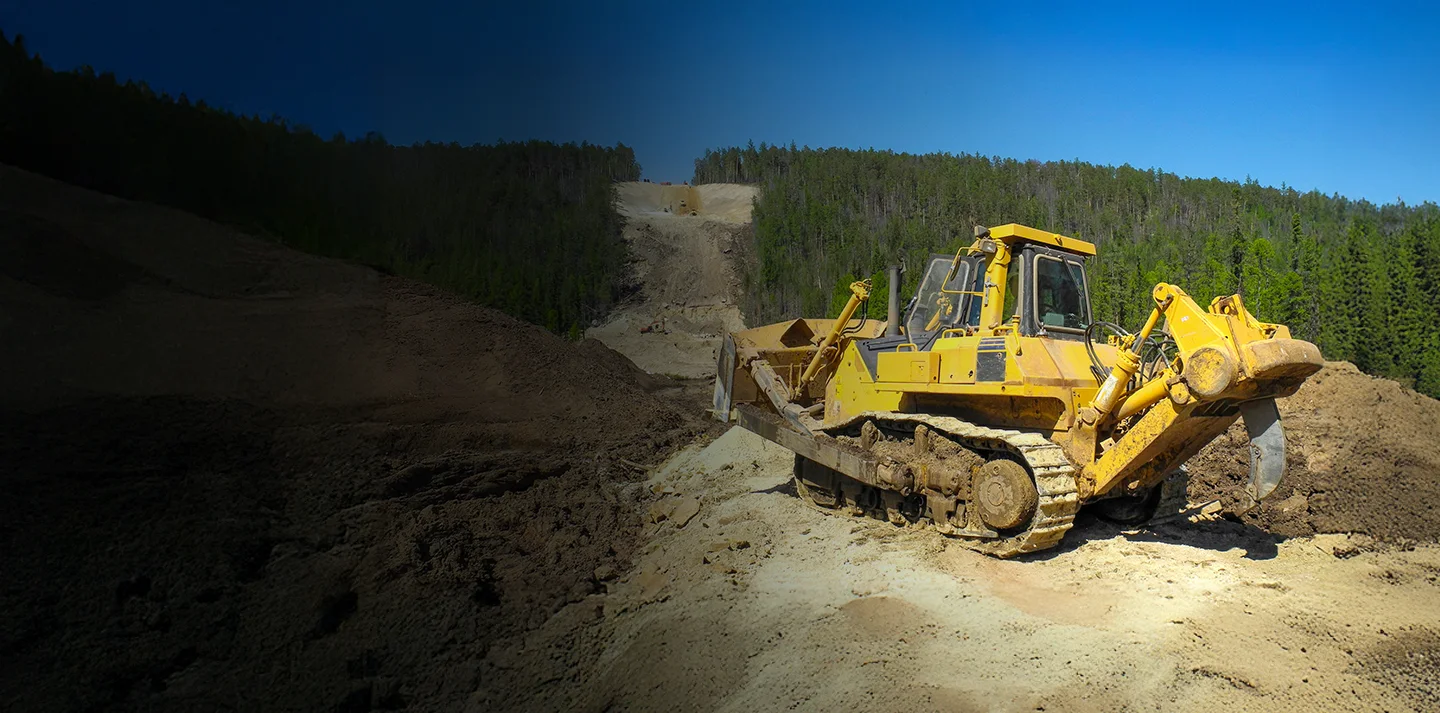 An excavator parked next to a large rocks at construction site out in the woods