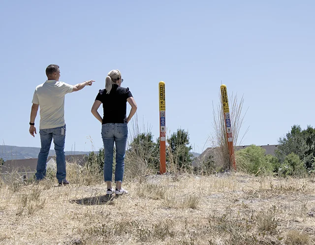 Two people pointing out yellow pipeline markers while walking through desert brush