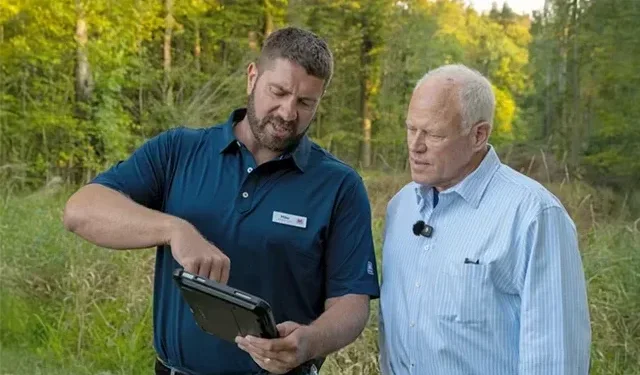 A Marathon Pipe Line employee showing a landowner where pipelines are located on their property with a small tablet while they walk through the woods