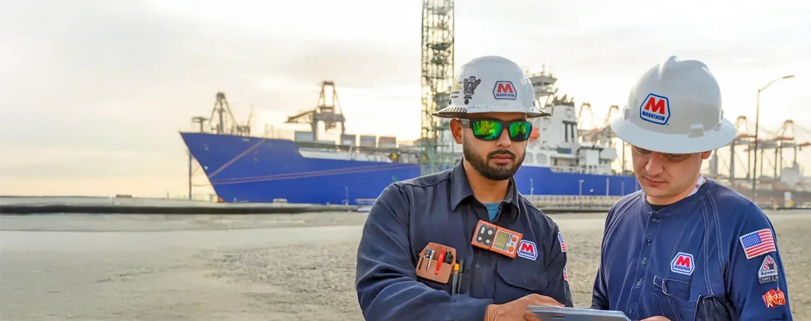 Two MPL dock workers reviewing paperwork on a clipboard with a large tanker in the background