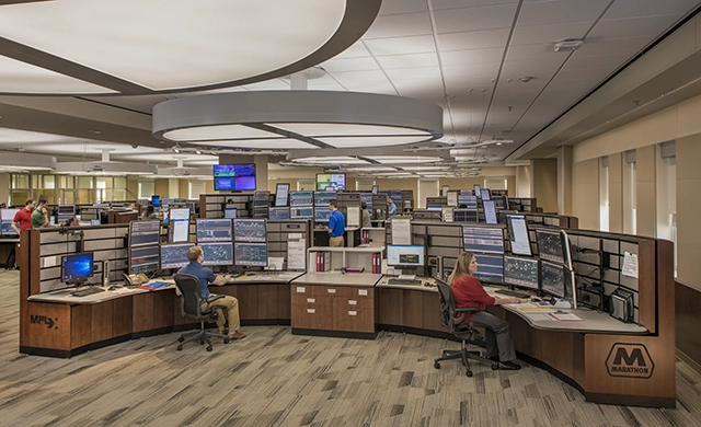 A pipeline control room with multiple operators working at curved desks filled with monitors displaying data and system controls, inside a modern Marathon Petroleum facility