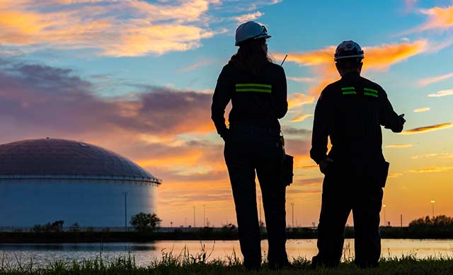 Two MPL employees looking at gas storage tanks across an inlit at sunset